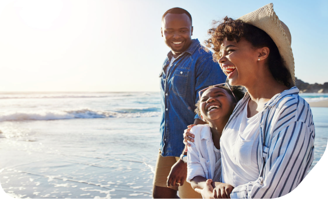 A husband and wife walk with their daughter on a sunny beach